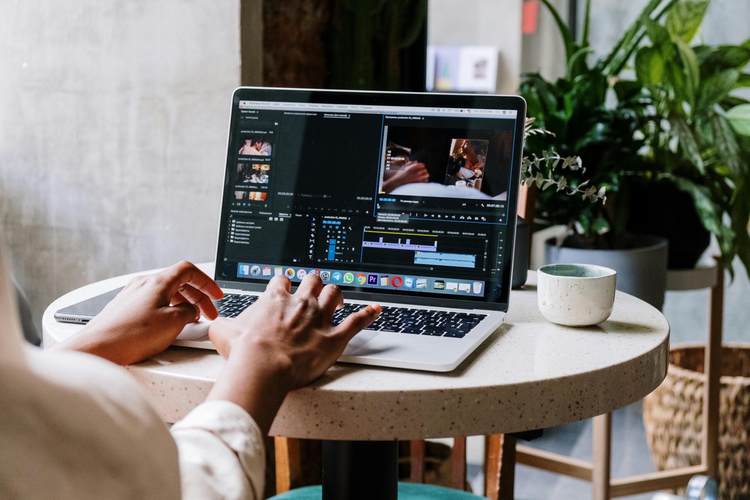 Freelance video editor working on a laptop in a cafe setting, utilizing Adobe software.